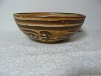 Side view of round studio pottery bowl displaying textured carved design in shades of brown