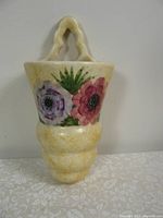 Front view of the yellowish vintage ceramic wall pocket with purple and pink flowers and double loop handle.