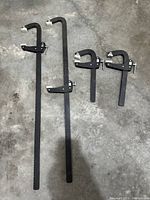 Four clamps laid out on a concrete floor: two large clamps measuring approximately 28 inches, two small clamps approximately 10 inches. Clamps are black metal with white plastic jaw pads.