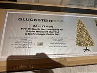 Photo of the box indicating the brand GlucksteinHome, product details such as 7 ft height, 400 warm white LED lights, 1705 tips, hinged construction and folding metal stand included.