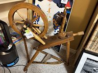Front view of the wooden spinning wheel showing the large wheel, pedal, and spindle assembly.