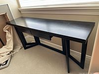 Full view of black wood sofa table by a window showing rectangular flat top and geometric leg design.