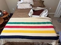 Hudson's Bay blanket displayed on a bed with two additional folded blankets in the background