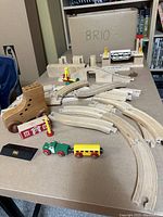 Train set pieces laid out on table showing curved and straight tracks, bridge, train engine and passenger car, signal pieces and switches.