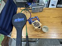 Photo showing Prince Extender badminton racquet and cover, Panasonic radio on a table with wooden boxes and ceramic cup.
