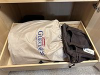 Photo showing Coleman GuestRest air bed in beige storage bag and dark brown hand bag placed next to each other inside a drawer.
