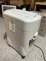 White Royal brand paper shredder angled from front left side showing body and control panel on top. The device has wheels for mobility and a worn appearance.
