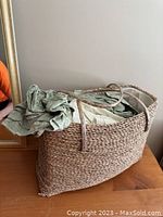 Wicker basket containing bedding sheets, shown from the side with basket handles visible.