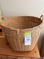 Front view of a large round wicker laundry basket with a woven pattern and handles on each side, placed on a wooden surface.