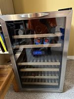 Front view of wine fridge showing glass door, wooden shelves, bottles and digital temperature display