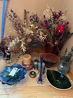 Overview of lot items: bowls of various colors and shapes, hand blown vases, candles, and faux flower arrangements.