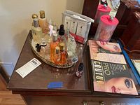 Photo showing mirrored vanity tray with several perfume bottles, unopened Nioxin scalp treatment packets, cosmetic books, and nail polish on wooden surface.