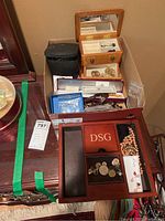 Photo shows assorted jewelry and jewelry boxes arranged in boxes sitting on a wooden cabinet surface. Includes pins, buttons, earrings, necklace, and various jewelry boxes of wood, vinyl and paper.