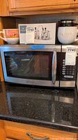 Emerson microwave on a kitchen counter with items on top including Godiva container and box of kitchen gadgets. Shows overall exterior and condition of microwave.