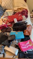 Photo showing assorted handbags, purses, wallets and costume jewelry arranged on a soft surface.