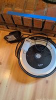 Photo showing the iRobot Roomba floor cleaner with charging dock placed on wooden floor near fireplace.