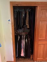 Closet interior showing two hanging rods filled with various men's clothing including pants and shirts in darker and neutral colors.