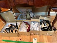 Five pairs of Michael Kors women's dress shoes displayed inside their respective boxes on wooden floor under a wooden furniture piece.