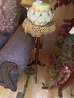 Photo of tall wooden stand with crocheted doily, decorative floral candle holder with beige candle on top, large ornate metal key on floor next to stand.