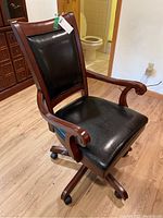Front view of wood framed swivel office chair showing black leather-like padded backrest and seat with wooden arms and five caster wheels.