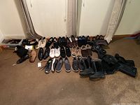 Overview photo of all shoes in lot showing multiple pairs of men's and women's shoes including boots, dress shoes, casual shoes, and sneakers arranged on carpet floor.