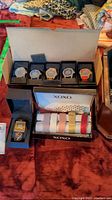 Five wristwatches and XOXO watch bands displayed on red fabric
