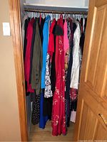 Photo of a closet rod filled with multiple women's dresses and clothing on hangers, various colors and styles visible.