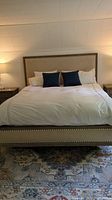 Front view of the California king bedframe with headboard, white bedding, two navy blue pillows, and bedside lamps.
