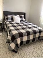 Full view of bed showing gray upholstered platform frame and headboard with checkered quilt and pillows.