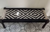 Full view of black and white woven bench with wooden legs on patterned tile floor.