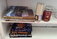 Shelf with six hardcover books and two candles displayed, showing titles and candle types.