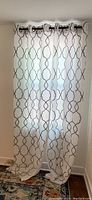 Full view of one pair of curtains hanging from one curtain rod with black end caps, white fabric with brown embroidered geometric pattern, length approximately 94 inches.