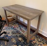Side view of farmhouse style wooden desk set on a patterned rug, showing rectangular top and leg supports.