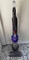 Front view of the Dyson DC50 Ball Compact upright vacuum cleaner in purple showing the handle, dust canister, ball base, and motorized brush head on patterned tile floor.