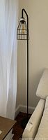 Full view of black metal floor lamp with cage shade, standing next to a sofa and curtain.