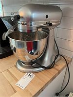 Full view of silver KitchenAid Artisan stand mixer with bowl attached on kitchen counter and power cord coiled beside.