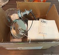 Photo showing two wall sconces in a cardboard box with parts including mounting plate and clear glass shade.