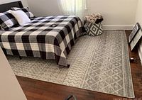 Photo showing the full beige and grey area rug under a bed with patterned blankets and pillows, highlighting the geometric and traditional designs.