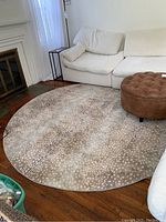 Photo of round Surya rug laid on hardwood floor next to white couch and brown ottoman, showing overall size and setting.