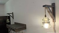 Wall sconces installed side by side on a white wall, lit and showing glass shades resembling insulators and metal bracket mounts.