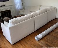 Back view of five modular sections arranged in L-shape on hardwood floor with rolled rug nearby