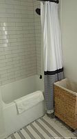 Photo showing white shower curtain with black and white stripes at bottom next to woven hamper.