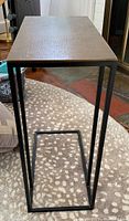 Front view of the black metal frame and brass top side table on patterned carpet.