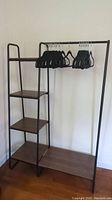 Full view of the freestanding metal clothes rack with four wood-look shelves and a hanging rod, with black and white hangers on it.