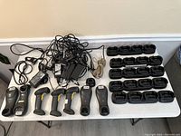 Table with multiple Honeywell handheld barcode scanners, several black charging bases, power adapters, and cables assorted together.