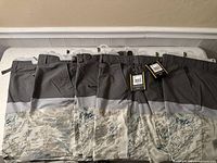 Six Mirage brand men's shorts hung on a wall-mounted rack. The shorts have dark gray upper sections and gray camouflage lower sections. Two pairs have tags visible.