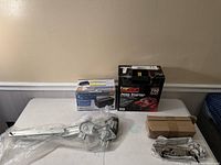 Four items set on table including EverStart jump starter, Tripp Lite battery backup, and two automotive window regulator mechanisms wrapped in plastic.