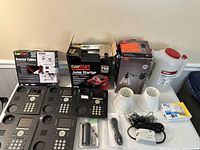 Overall view of the lot showing EverStart booster cables, jump starter box, two white lamp shades, assorted electronic devices, and a white plastic container with red lid.