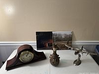 Front view of all five items on a table against a beige wall, showing clock, vase, airplane model, and vinyl records