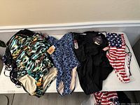 Multiple one-piece swimsuits laid out showing different colors and patterns including black, blue geometric, multi-color abstract and American flag print.